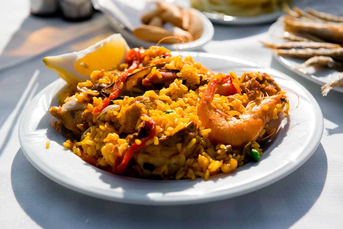 A white dish with mixed paella made with prawns and meat.