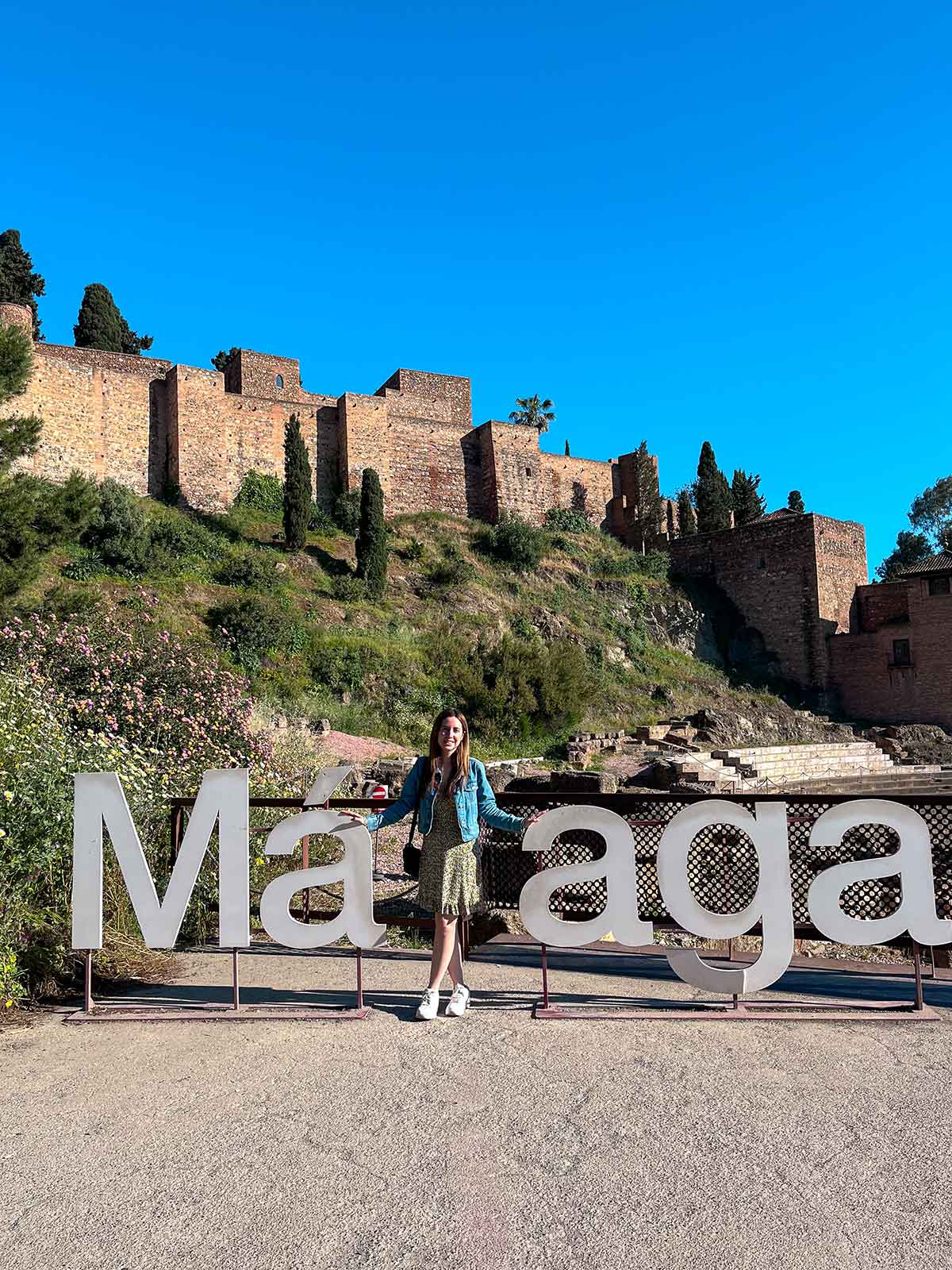 24 Best Malaga Instagram Spots By a Local 7 Cristina posing next to the Malaga sign overlooking the alcazaba fortress palace.