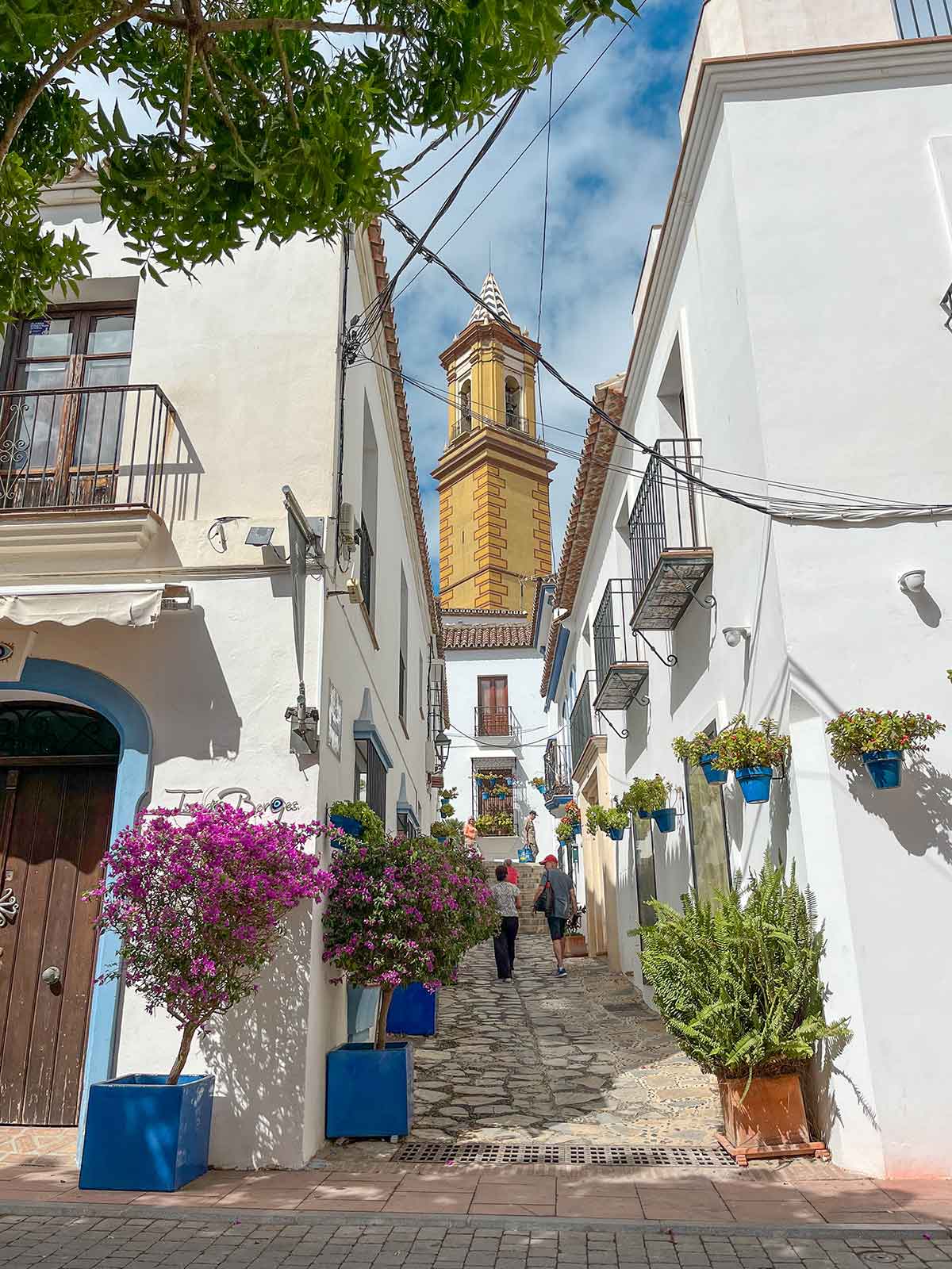 A street in Estepona old town with a view of a church tower and white painted buildings.