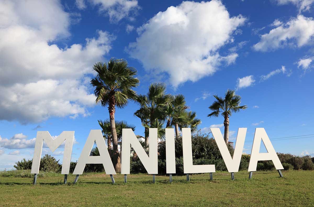 A sign in a roundabout with palm trees that reads Manilva.