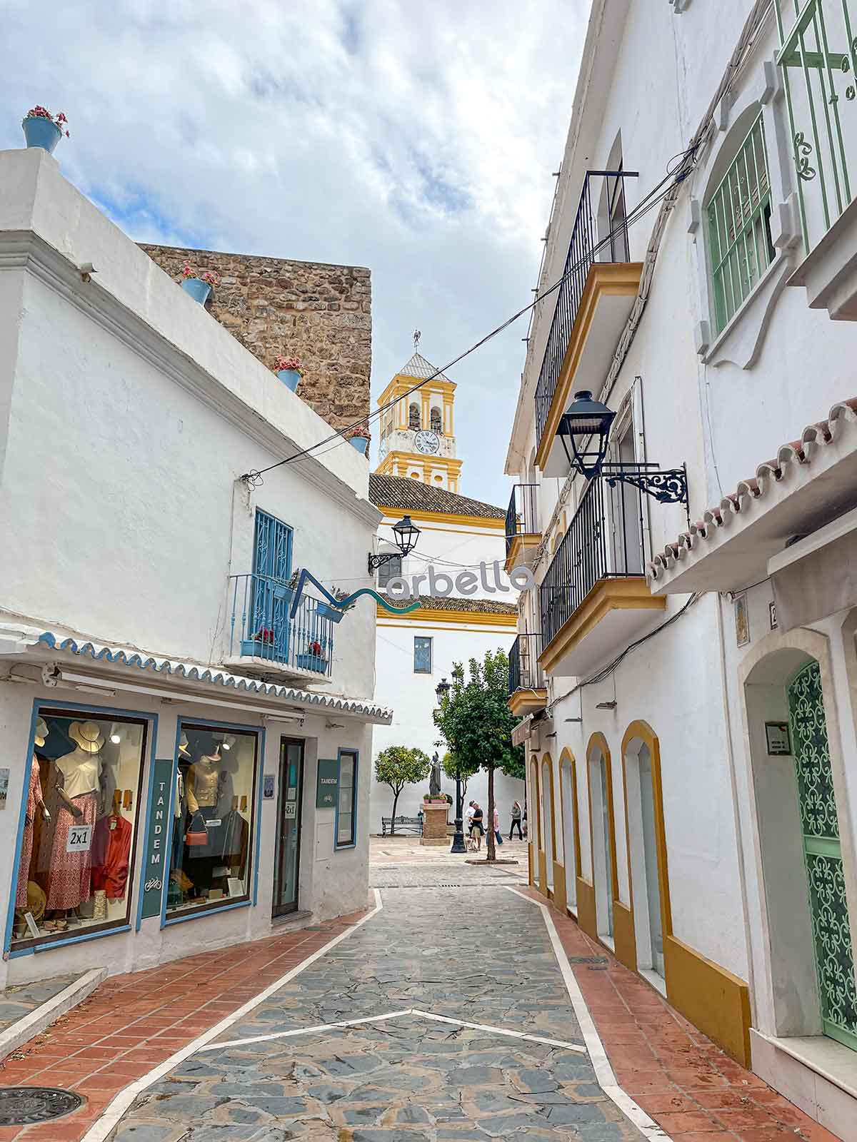 A photo taken from Carmen Street in Marbella Old Town, You can see the church tower at the end and shops at both sides of the street.