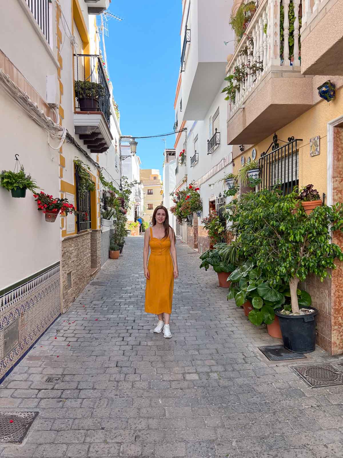 Cristina walking down a picturesque street with plants in Almunecar Old Town.