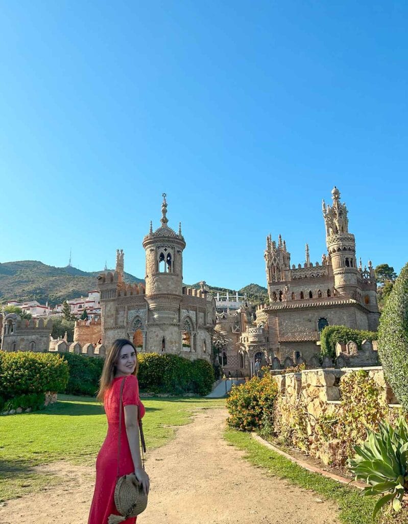 A woman wearing a long red dress posing in front of Colomares Castle, Benalmadena.