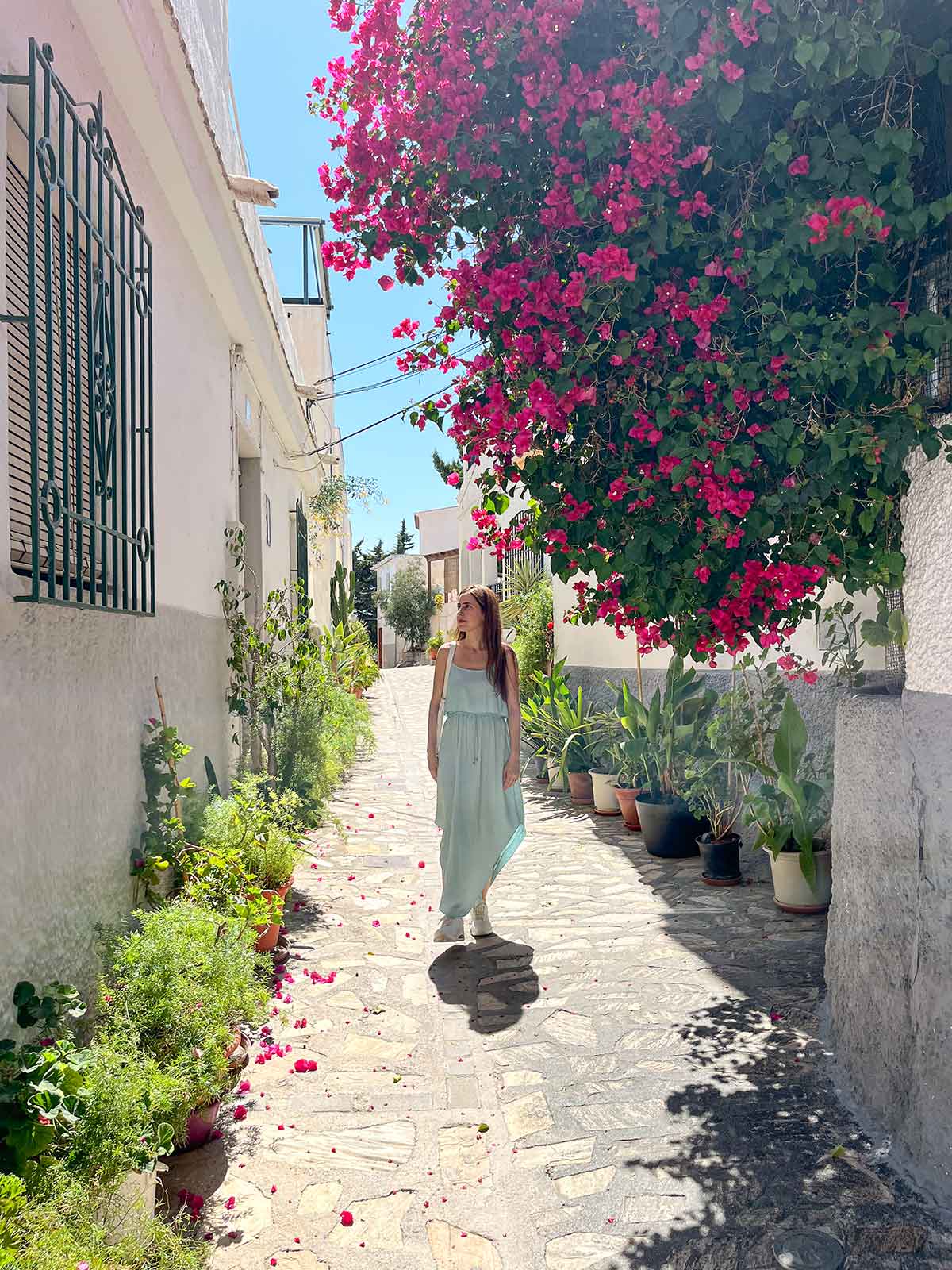 A woman wearing a turquoise long dress walking down a pretty street in Salobreña, Spain.