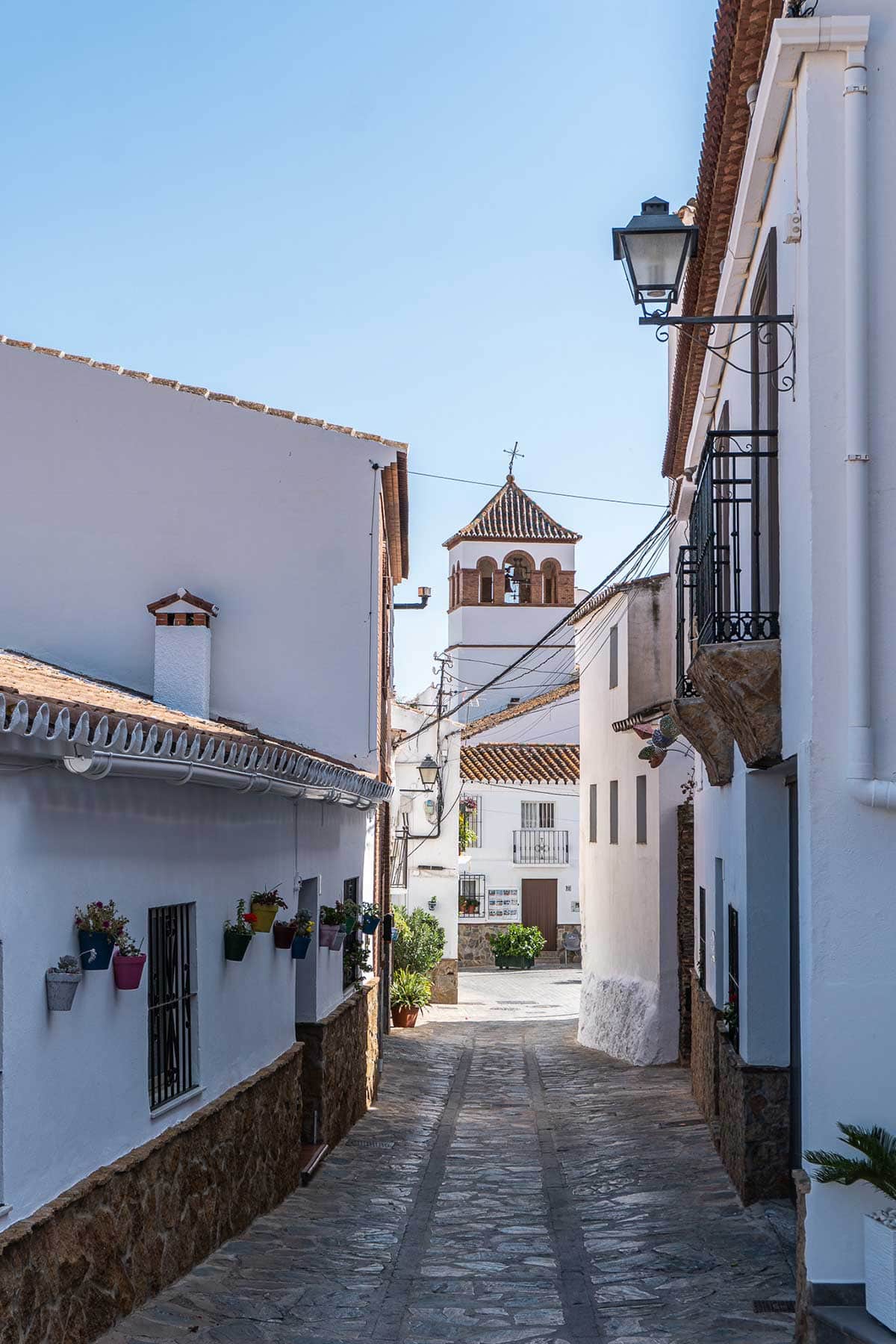 The view of a cobblestone street and the tower church of Moclinejo.