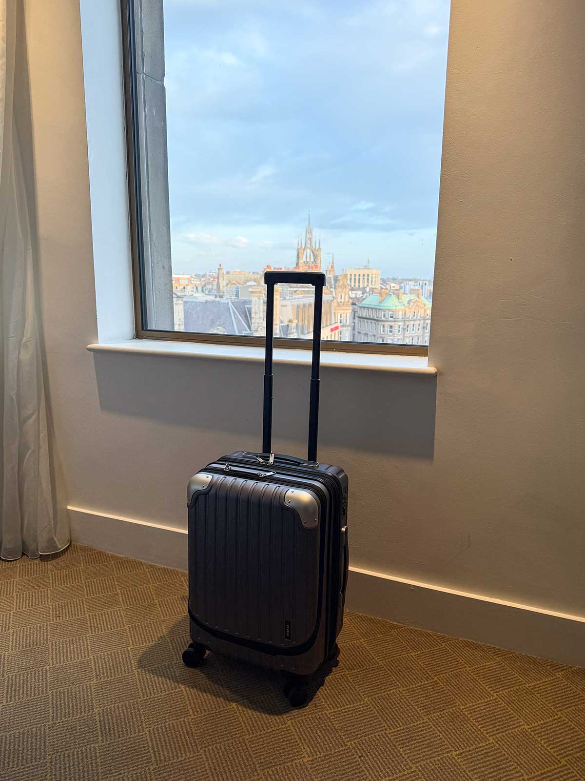 LEVEL8 Grace Carry-on Luggage Review 4 A photo of the LEVEL8 Grace carry-on luggage in a hotel room with a city view.