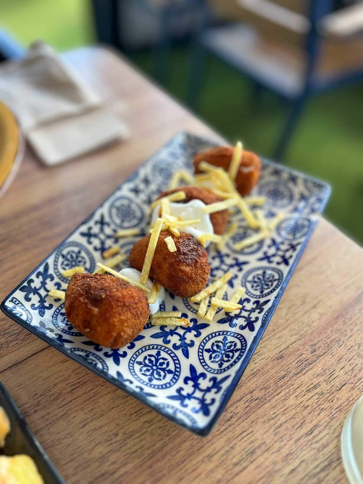 Croquetas served with ailioli and crisps in a tiled dish.