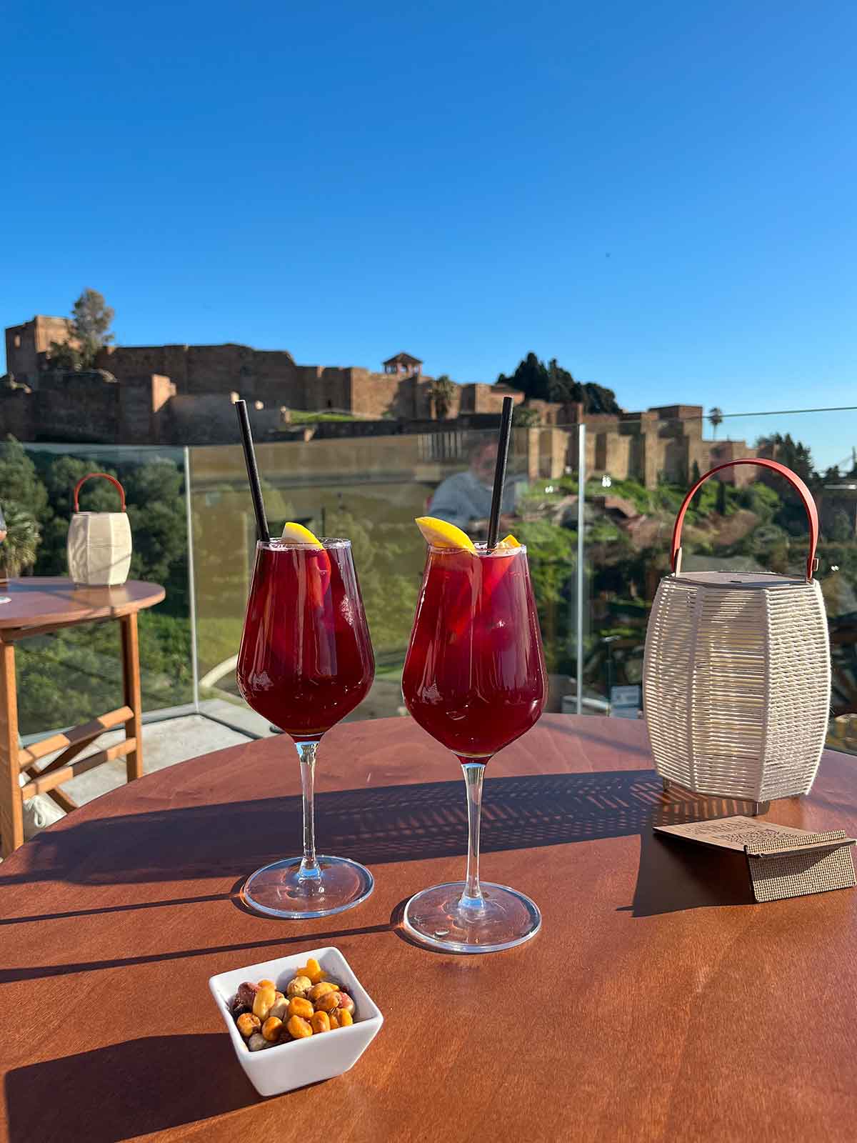 Two glasses of sangria and a small plate with nuts on a table served at the ME Malaga Hotel rooftop which has views of the Alcazaba fortress.