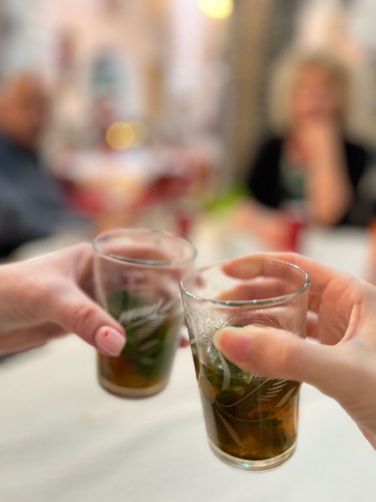 A close up photo of two hands holding a glass with Moroccan mint tea.
