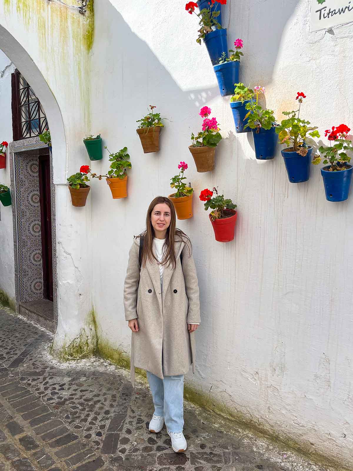 A woman posing next to a white painted wall decorated with flower pots in Tetouan, north Morocco.
