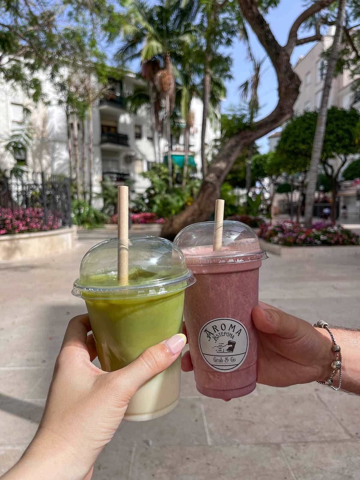 Where to Eat in Estepona (My Top Recommendations) 8 A close up photo of two hands holding an iced coconut matcha and a chocolate and strawberry milkshake from Aroma Grab and Go in Estepona.