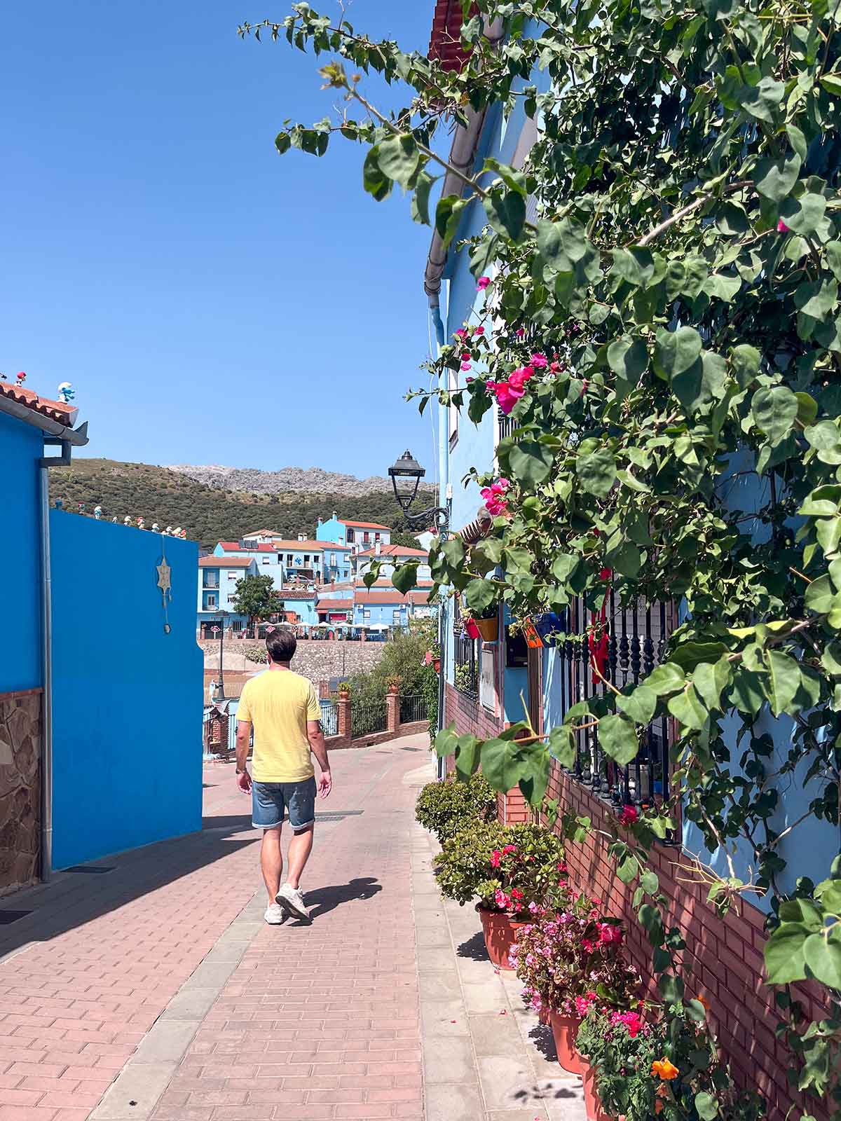 Things to Do in Juzcar, The Blue Village in Malaga 10 Man wearing shorts and yellow t-shirt walking down a street in juzcar, the smurf village, malaga, spain.