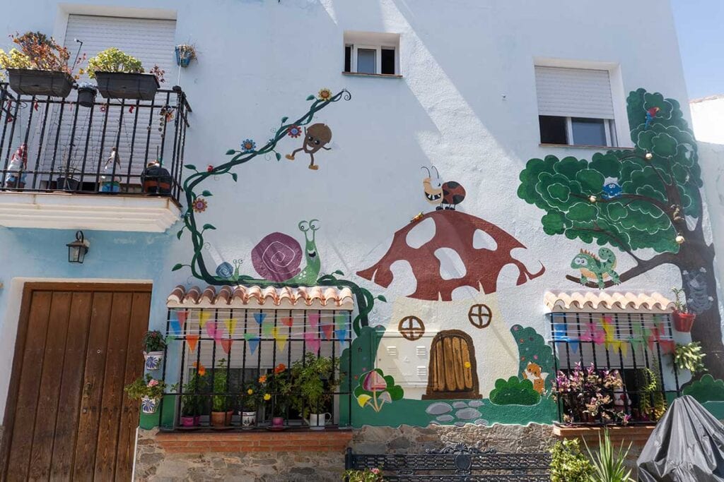 Things to Do in Juzcar, The Blue Village in Malaga 9 Mushroom shaped house and trees painting in a street in Juzcar.